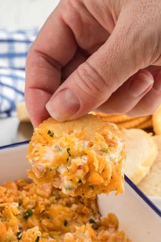 a hand holding a cracker over a casserole dish