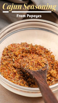 a glass bowl filled with spices next to a wooden spoon on top of a table