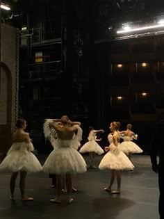 dancers in white tutus and feathered skirts on stage with one man standing behind them