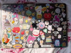 a laptop covered in lots of stickers on top of a white sheet with pink flowers