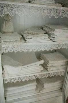 white linens are stacked on shelves in a closet with lace trim around the edges