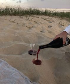 a person pouring wine into two glasses in the sand