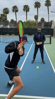 two men are playing tennis on a blue and green court with palm trees in the background