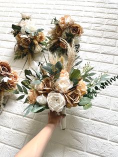 a person holding a bouquet of flowers in front of a white brick wall with greenery