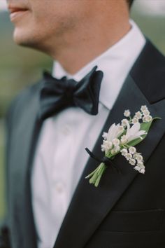 a man in a tuxedo with white flowers on his lapel and black bow tie