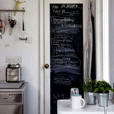 a kitchen with a chalkboard on the door and potted plants next to it