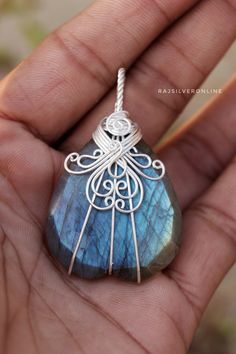 a hand holding a wire wrapped pendant with blue labradorite stone in the shape of a cage