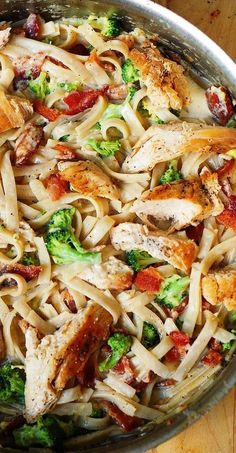 a pan filled with chicken, broccoli and pasta on top of a wooden table