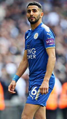 a man in blue uniform playing soccer on a field with people watching from the stands