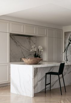 a modern kitchen with marble counter tops and white cabinets, along with a black chair