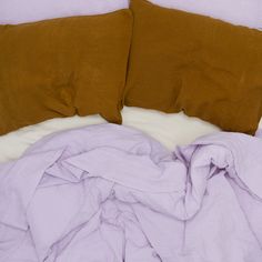 an unmade bed with purple sheets and brown pillows