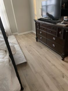 a bedroom with a bed, dresser and television on it's stand in front of a window