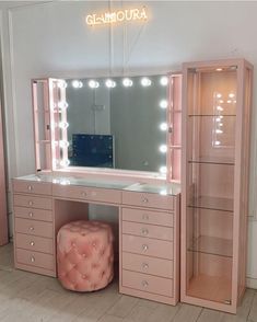 a pink vanity with lights on it and a stool in front of the mirror that is lit up