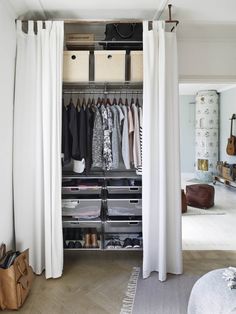 an open closet with white curtains and clothes