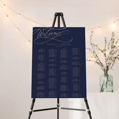 a black and white wedding seating chart on an easel with lights in the background