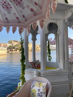 an outdoor gazebo next to the water with pink flowers and greenery on it