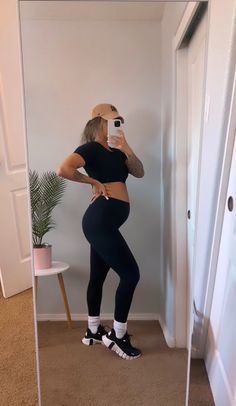 a woman taking a selfie in a mirror wearing leggings and sports shoes