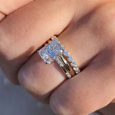 a woman's hand holding an engagement ring with three stones on it and one stone in the middle