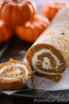 a cinnamon roll is cut in half and sitting on wax paper next to some pumpkins