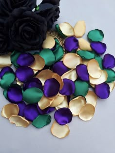 purple, green and gold petals are scattered next to a black rose