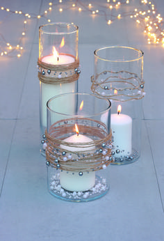 three candles are sitting in glass vases on the ground