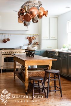 an island in the middle of a kitchen with pots and pans hanging from it