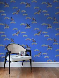 a chair sitting in front of a blue wallpaper with birds flying over the top