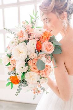 a bride holding a bouquet of peach and white flowers with greenery in her hair