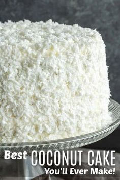 a white cake with coconut on top sitting on a glass platter that says, best coconut cake you'll ever make