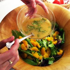 a person pouring dressing into a salad in a wooden bowl