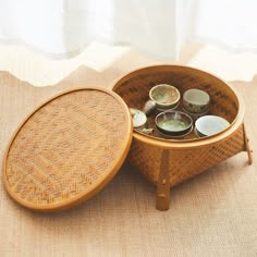 a wooden tray with some cups in it on top of a table next to a window