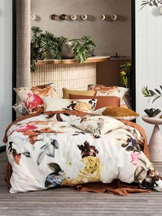 a bed covered in lots of pillows next to a potted plant on top of a wooden floor