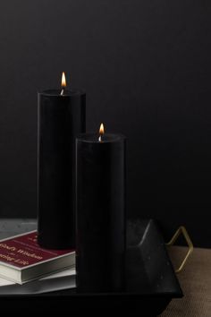 two black candles sitting on top of a table next to a book and candle holder