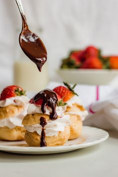 chocolate sauce being drizzled over strawberry shortcakes on a white plate