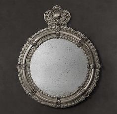 an ornate silver framed mirror on a black wall in the shape of a round frame