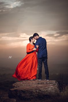 a man and woman standing on top of a rock in front of a cloudy sky