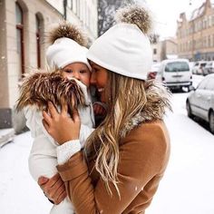 a woman holding a baby in her arms while standing on the side of a snow covered street