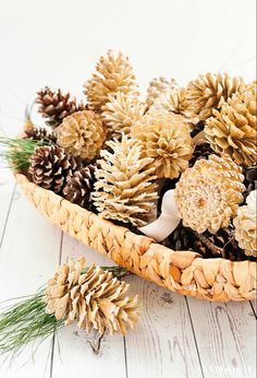 some pine cones are in a basket on a white wooden table and one is laying down