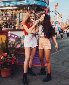 two young women standing next to each other near a food stand and eating ice cream