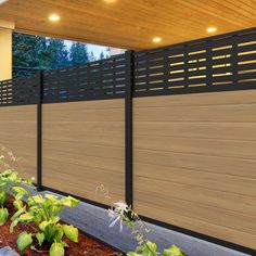 a wooden fence next to a house with plants growing on the ground in front of it