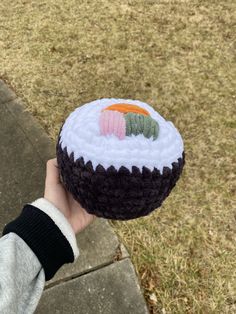 a person holding up a small sushi cake on the sidewalk in front of some grass