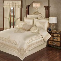 a bed with white and gold comforters in a bedroom next to a window,