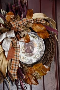 a wreath that is hanging on the front door with autumn leaves and a plate in it