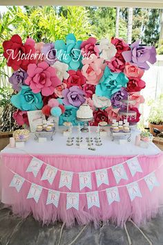 a table topped with cake and cupcakes covered in pink and blue paper flowers