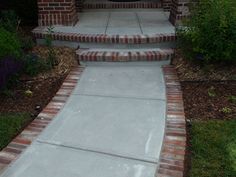 a cement walkway with brick steps leading up to the front door