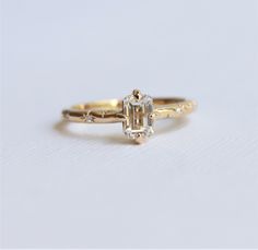 a yellow gold ring with an emerald cut diamond in the center and two small diamonds on each side