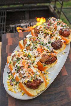 hot dogs with toppings sit on a plate in front of an open fire pit