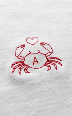 a crab embroidered onto a white t - shirt with the letter a in red thread