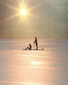 two people on surfboards in the middle of water with sun shining down over them