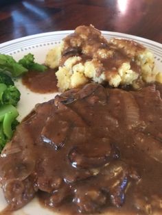 a white plate topped with meat and gravy covered in gravy next to broccoli